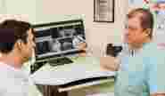 Врач показывает пациенту его снимок КТ на компьютере